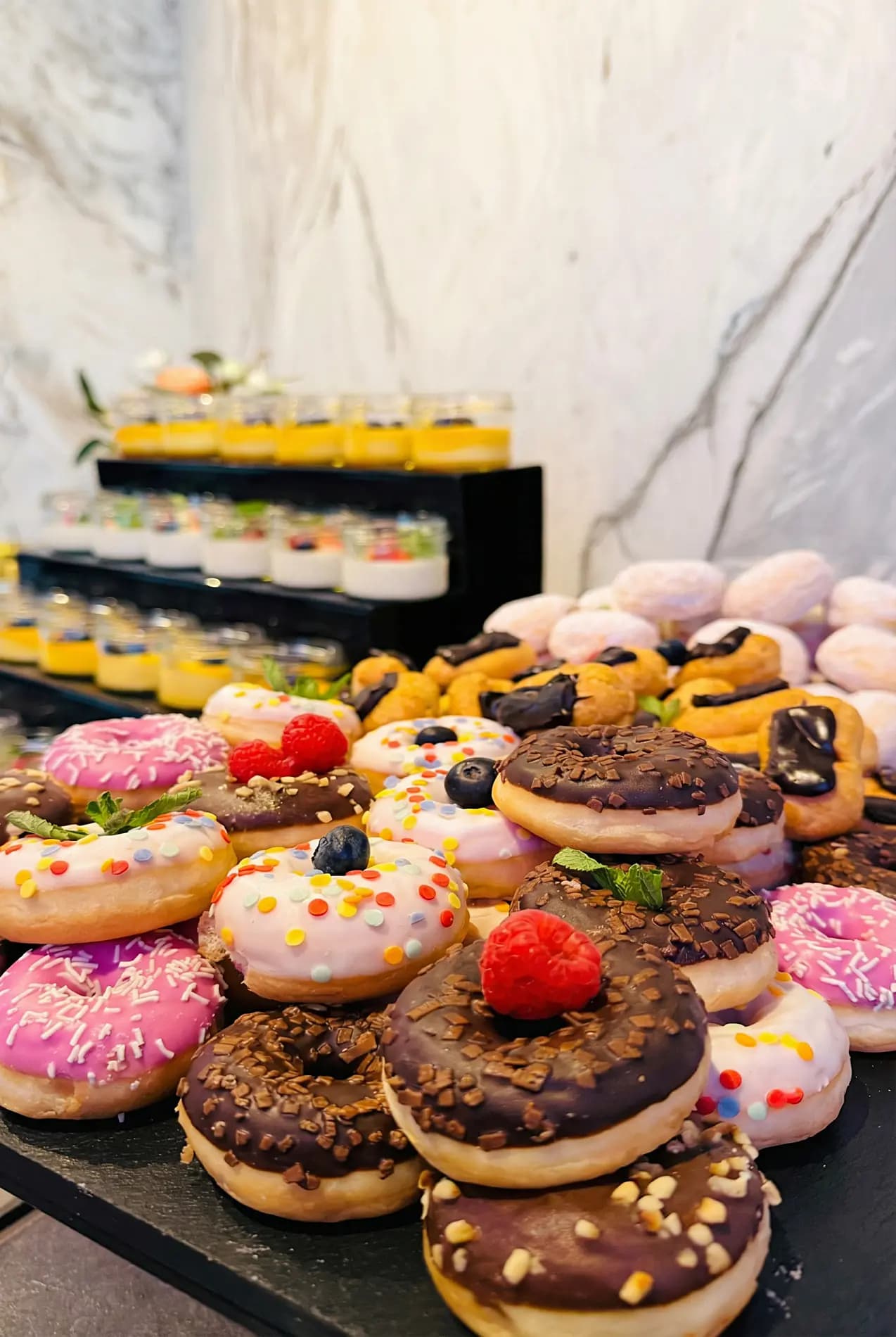 Stół deserowy — kolorowe donuty, petit fours i desery w szklankach